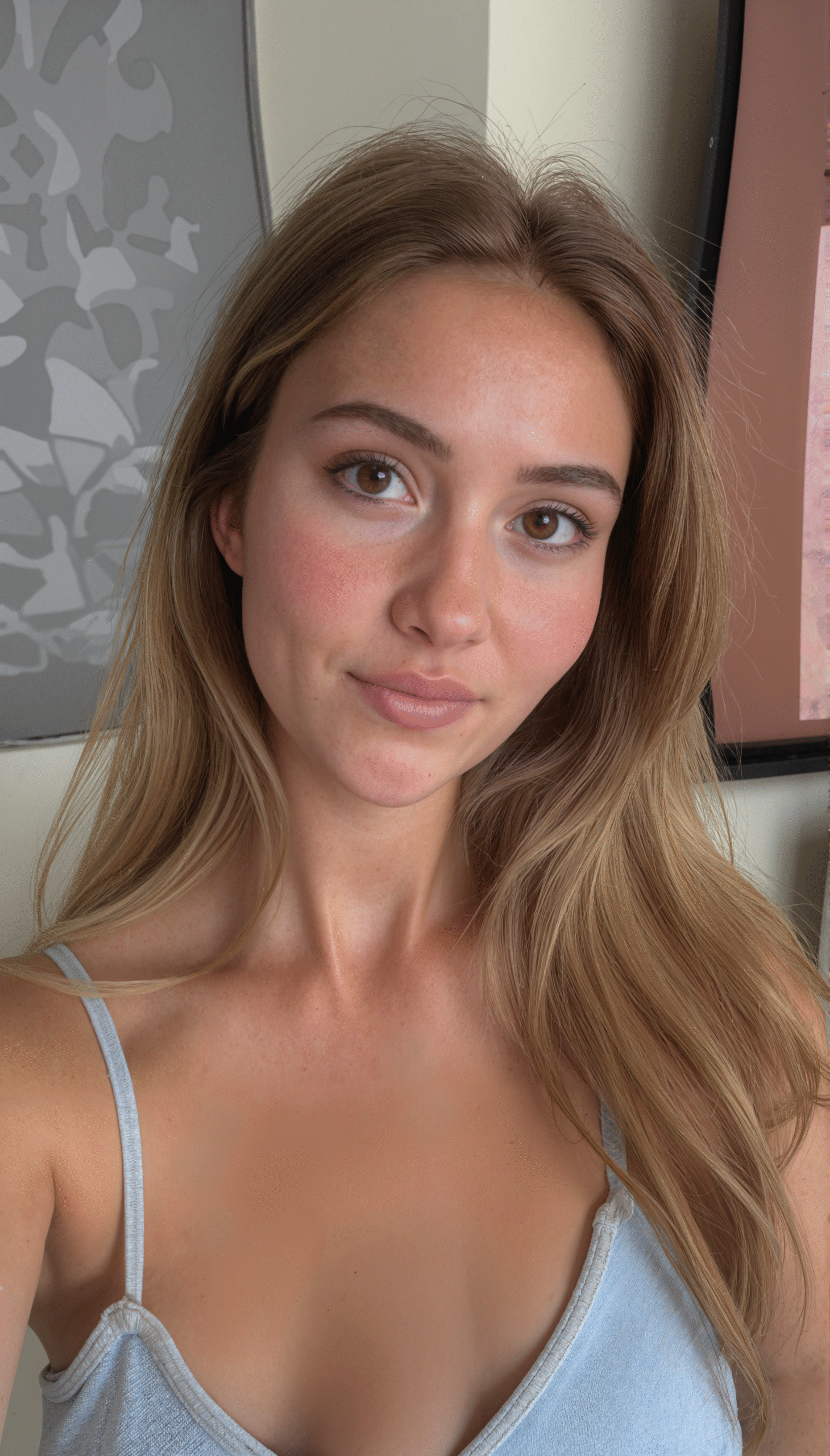 Woman with natural makeup and light blue top taking a selfie indoors